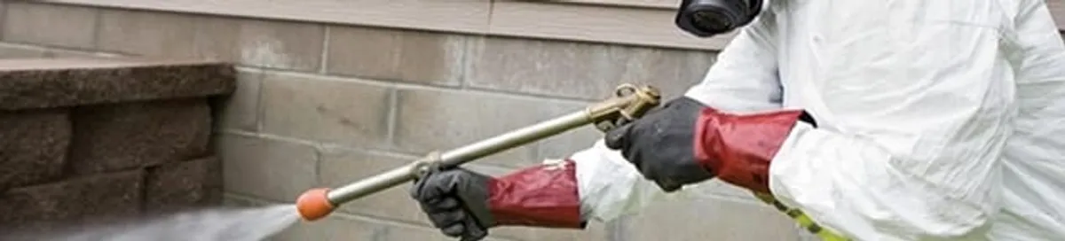 Pest control technician applying exterior insect treatment along a home foundation in San Francisco, CA