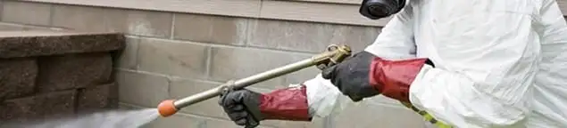 Pest control technician applying exterior insect treatment along a home foundation in San Francisco, CA