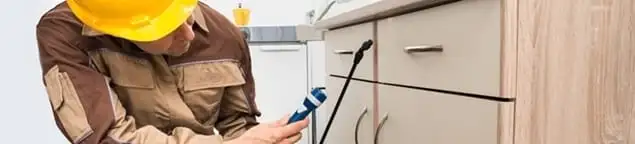 Roach exterminator applying treatment under kitchen cabinets in San Francisco, CA