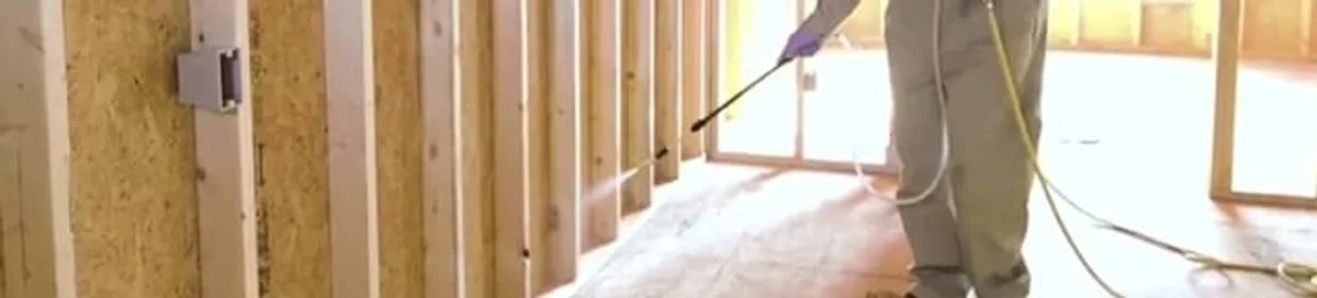 Termite treatment technician applying spray along framing and unfinished walls in San Francisco, CA