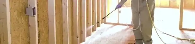 Termite treatment technician applying spray along framing and unfinished walls in San Francisco, CA